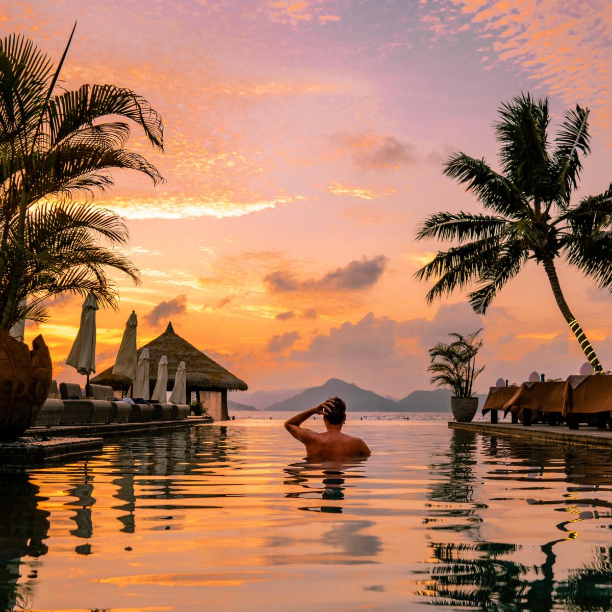 Luxury swimming pool in a tropical resort, relaxing holidays in Seychelles islands. La Digue, Young man during sunset by swim pool Seychelles